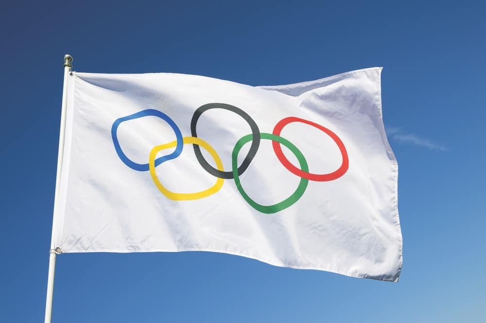 An Olympic flag flutters in the wind against bright blue sky in celebration of the city hosting the Summer Games